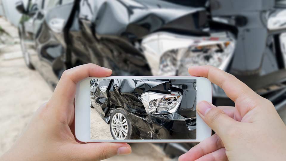Unfallwagenankauf Ulm: Unfallschaden an einem Auto wird mit dem Smartphone fotografiert.